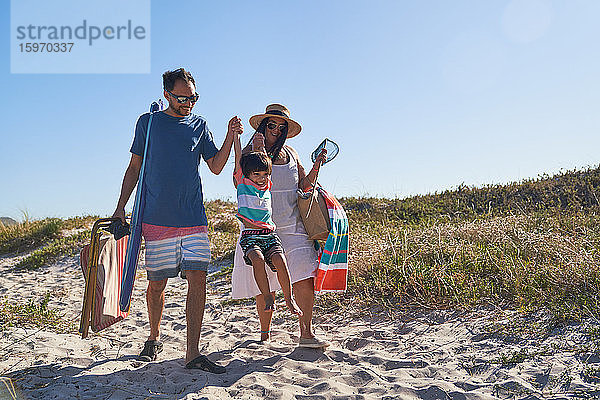 Verspielte Familie beim Spaziergang im Sand auf einem sonnigen Strandweg
