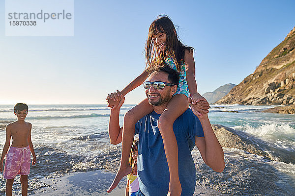 Glücklicher Vater trägt Tochter auf den Schultern am sonnigen Meeresstrand