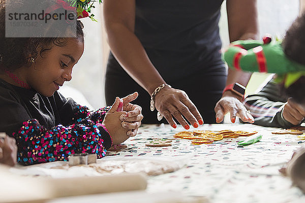 Mädchen schmückt Weihnachtsplätzchen mit der Familie am Tisch