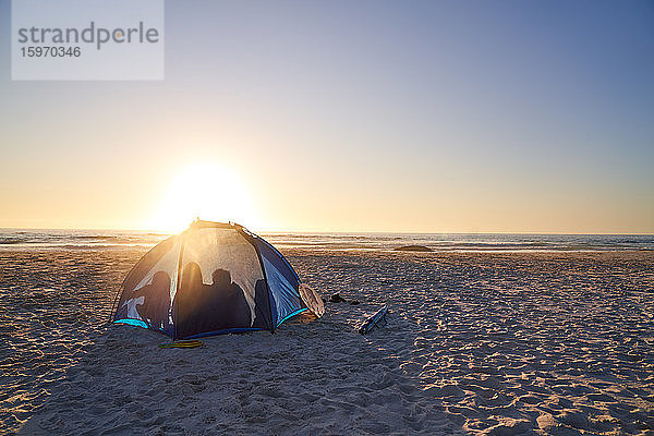 Silhouette der Familie im Zelt am sonnigen Strand bei Sonnenuntergang