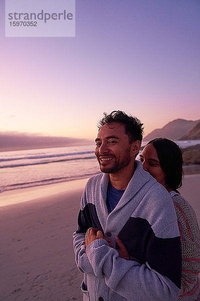 Liebespaar umarmt sich bei Sonnenuntergang am Meeresstrand