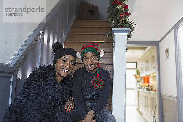 Porträt einer glücklichen Mutter und ihres Sohnes mit Weihnachtshüten auf der Treppe