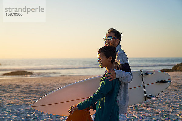 Vater und Sohn mit Surfbrett am sonnigen Strand