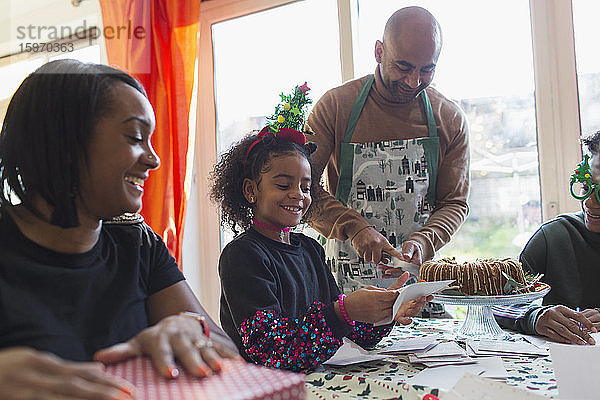 Glückliche Familie packt Weihnachtsgeschenke ein und schreibt Karten bei Tisch