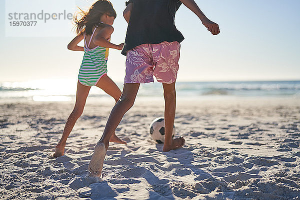 Bruder und Schwester spielen Fussball am sonnigen Strand