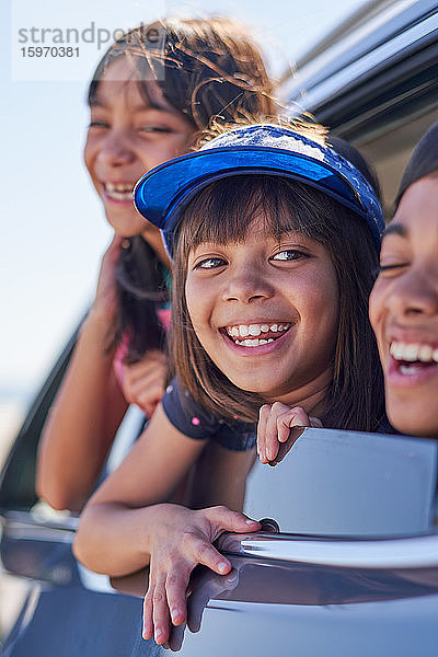 Glückliche Schwestern und Brüder lehnen sich aus dem sonnigen Autofenster