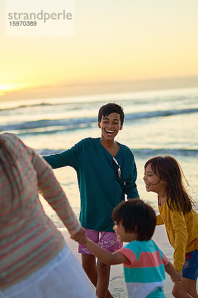 Glückliche Familie spielt am Strand bei Sonnenuntergang