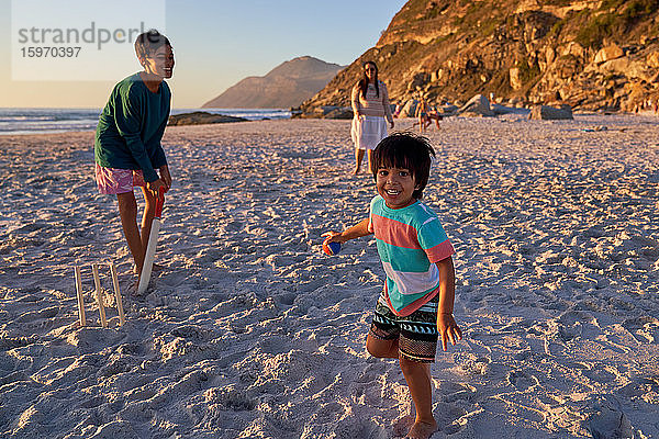 Porträt einer glücklichen Familie beim Kricketspielen am sonnigen Strand