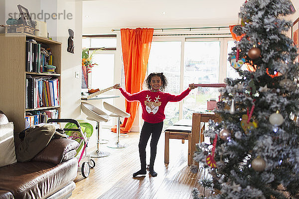 Porträt eines glücklichen Mädchens in Weihnachtspullover mit Geschenkpapier in der Hand