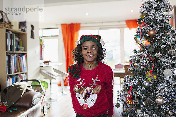 Porträt eines festlichen Mädchens in Weihnachtspullover und Hut am Baum