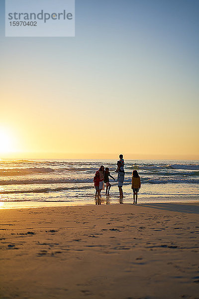 Familie watet bei Sonnenuntergang am Strand in der Brandung