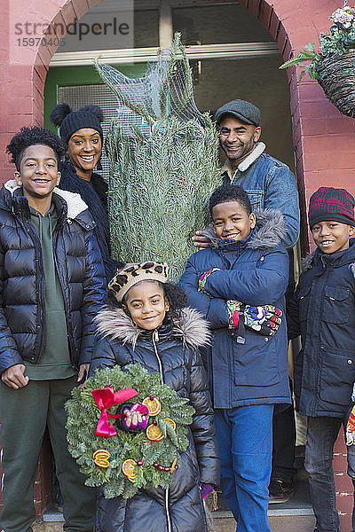 Porträt einer glücklichen Familie mit Weihnachtsbaum und Kranz auf der Vordertreppe