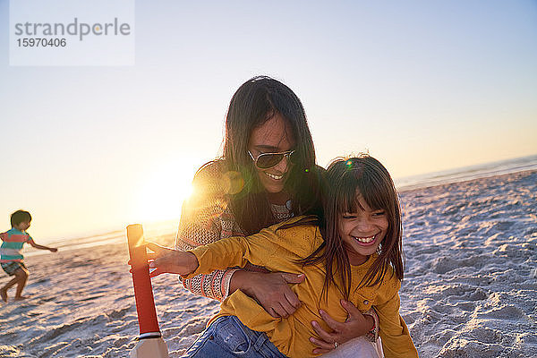 Glückliche Mutter und Tochter umarmen sich am Strand bei Sonnenuntergang