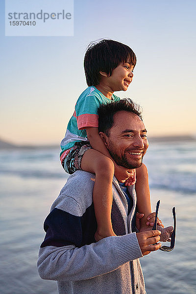 Glücklicher Vater trägt seinen Sohn auf den Schultern am Strand des Ozeans