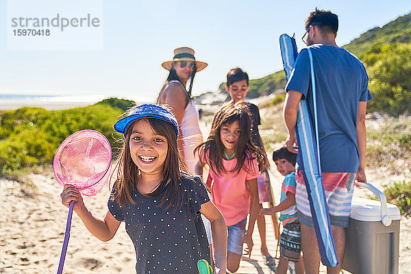 Porträt eines glücklichen Mädchens mit Schmetterlingsnetz am sonnigen Strand mit Familie