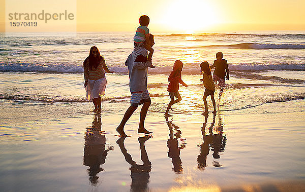 Familie watet bei Sonnenuntergang am idyllischen Meeresstrand in der Brandung