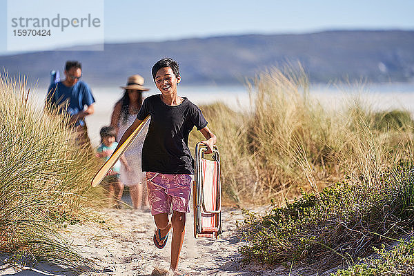Glücklicher Junge läuft mit Klappstuhl auf sonnigem Strandweg