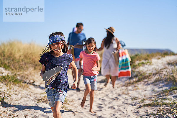 Glückliches Mädchen läuft mit Familie am sonnigen Strand