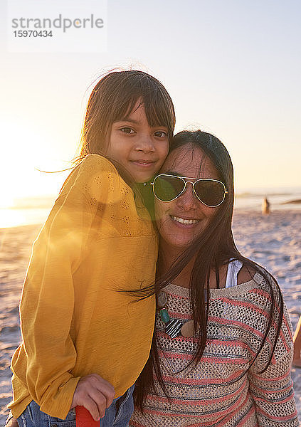 Porträt einer glücklichen Mutter und Tochter am sonnigen Strand bei Sonnenuntergang