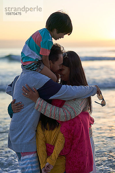 Liebevolle Familienumarmung am Meeresstrand bei Sonnenuntergang