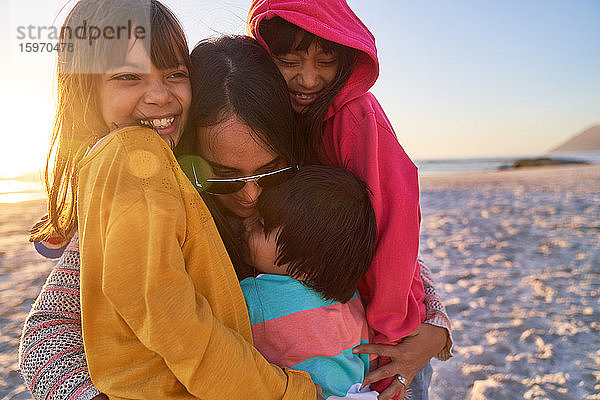 Glückliche Mutter und Kinder umarmen sich am sonnigen Strand