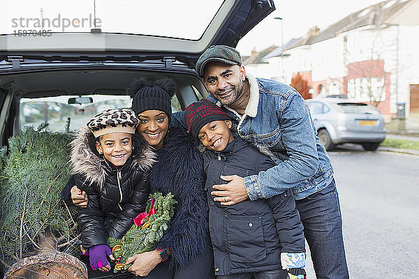 Porträt einer glücklichen Familie beim Verladen des Weihnachtsbaums auf dem Rücksitz eines Autos