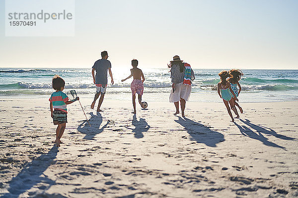 Familie läuft und spielt Fussball am sonnigen Meeresstrand