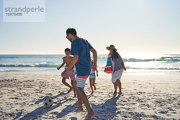 Familie spielt Fussball am sonnigen Meeresstrand