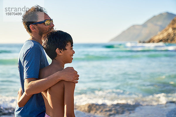 Liebevolle Umarmung von Vater und Sohn am sonnigen Meeresstrand