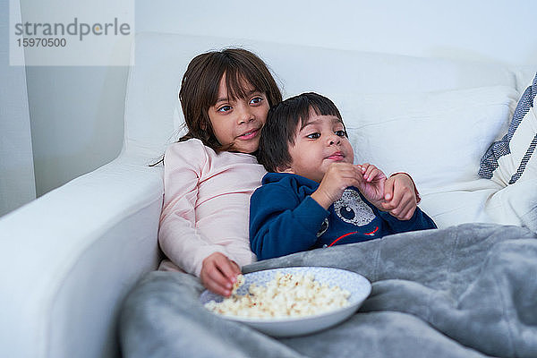 Liebevolle Geschwister essen Popcorn und sehen auf dem Sofa fern