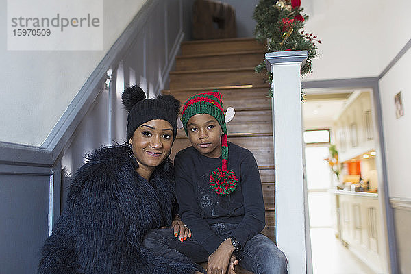 Porträt Mutter und Sohn mit Weihnachtshüten auf der Treppe zu Hause