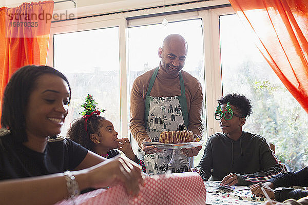 Der Vater serviert der Familie bei Tisch Weihnachtskuchen