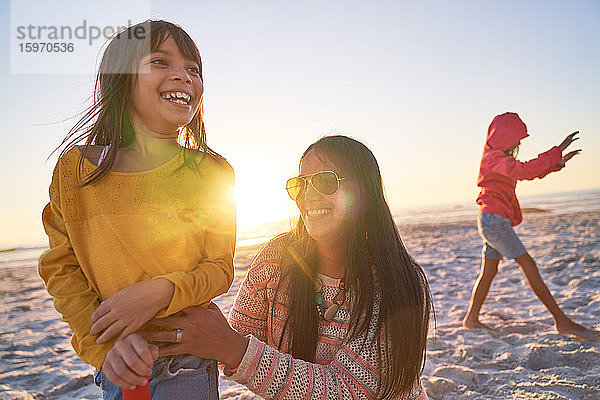Glückliche Mutter und Tochter spielen bei Sonnenuntergang am sonnigen Strand
