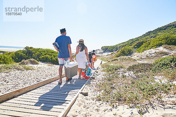 Familie trägt Ausrüstung auf sonniger Strandpromenade