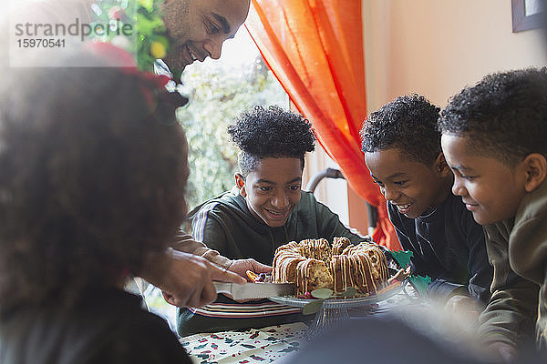 Der Vater serviert eifrigen Söhnen bei Tisch Weihnachtskuchen