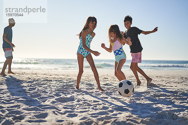 Glückliche Familie spielt Fussball am sonnigen Strand