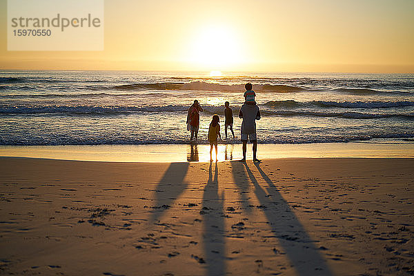 Familie watet im Sommer in der Brandung des Ozeans bei Sonnenuntergang
