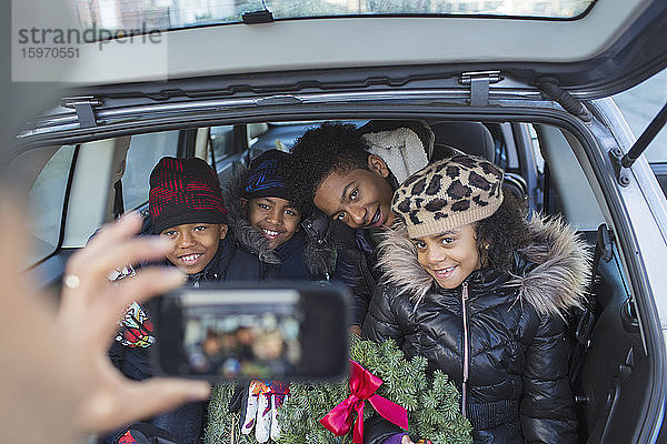 Glückliche Familie mit Weihnachtskranz  die im Auto für ein Foto posiert