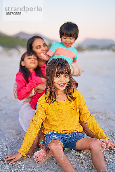 Porträt eines glücklichen Mädchens mit Familie im Sand am Strand