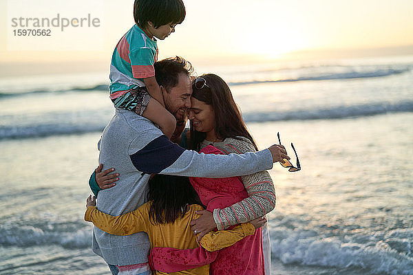 Glückliche  liebevolle Familie umarmt sich bei Sonnenuntergang am Meeresstrand