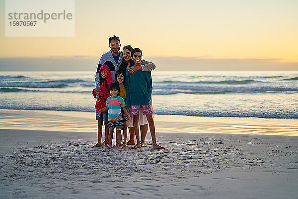 Porträt einer glücklichen Familie am Meeresstrand bei Sonnenuntergang