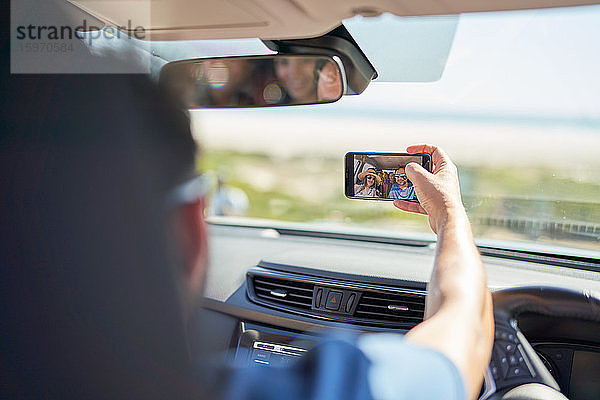 Familie auf Autoreise mit Selfie mit Fotohandy im sonnigen Auto