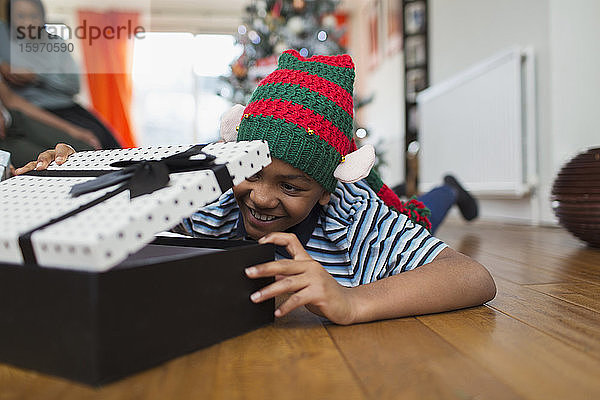 Aufgeregter Junge öffnet Weihnachtsgeschenk auf Wohnzimmerboden