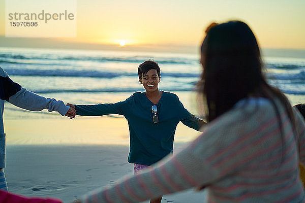 Glückliche Familie hält bei Sonnenuntergang am Strand des Ozeans im Kreis Händchen