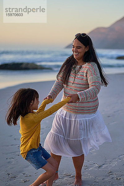 Verspielte Mutter und Tochter tanzen am Strand