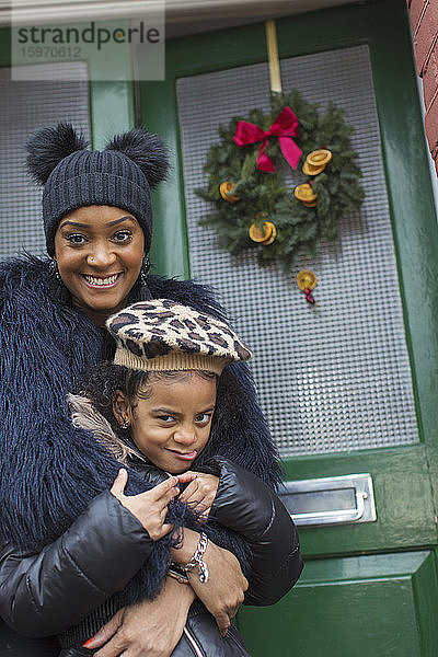 Porträt glückliche Mutter und Tochter vor der Haustür mit Weihnachtskranz