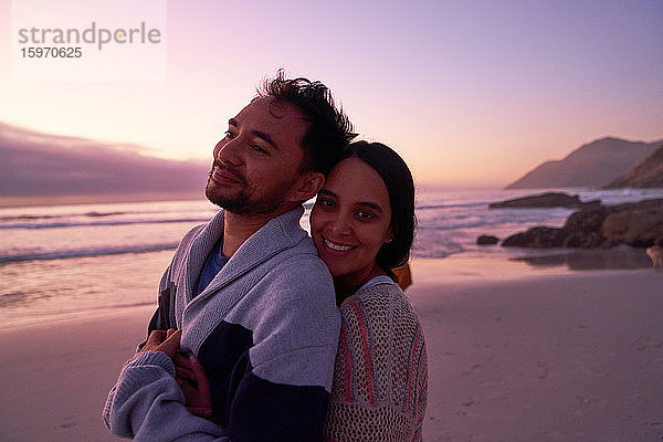 Porträt eines glücklichen  zärtlichen Paares  das sich bei Sonnenuntergang am Strand umarmt