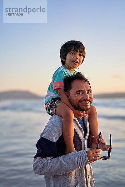 Porträt eines glücklichen Vaters  der seinen Sohn auf den Schultern am Strand trägt