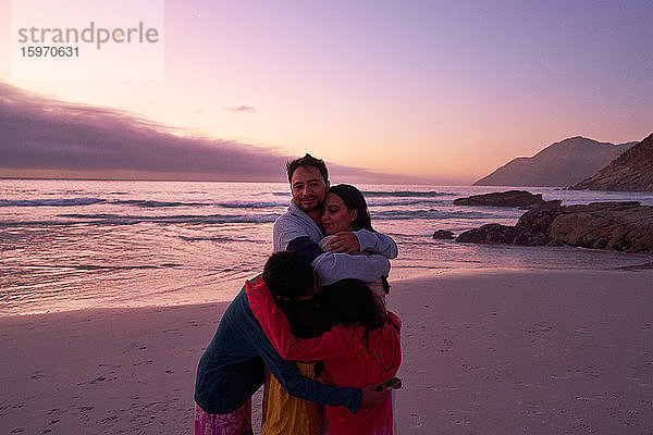 Porträt einer glücklichen Familie  die sich am Strand bei Sonnenuntergang am Meer umarmt  Kapstadt