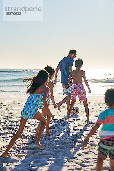 Familie spielt Fussball am sonnigen Meeresstrand